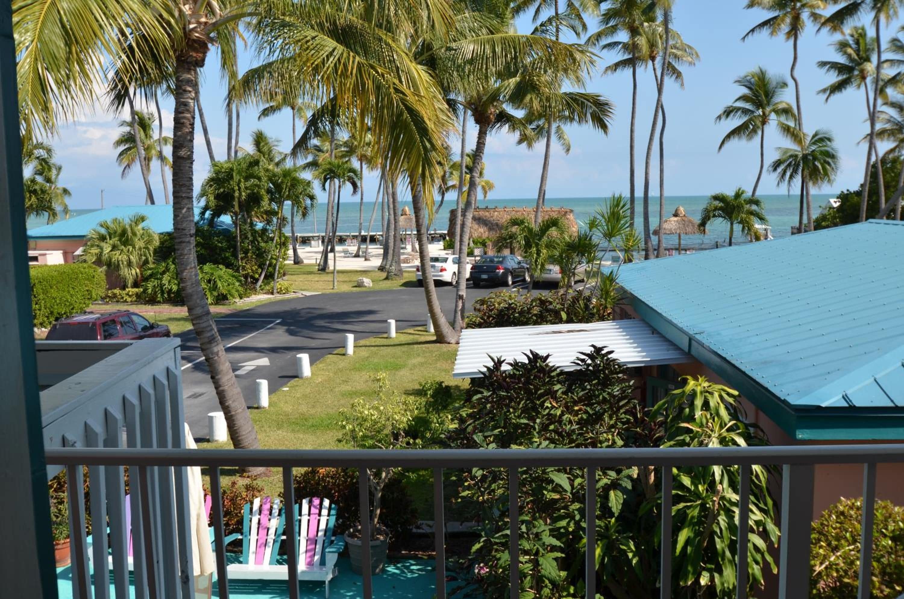 Vista de una propiedad frente a la playa con zona de estacionamiento, palmeras y cielo despejado.