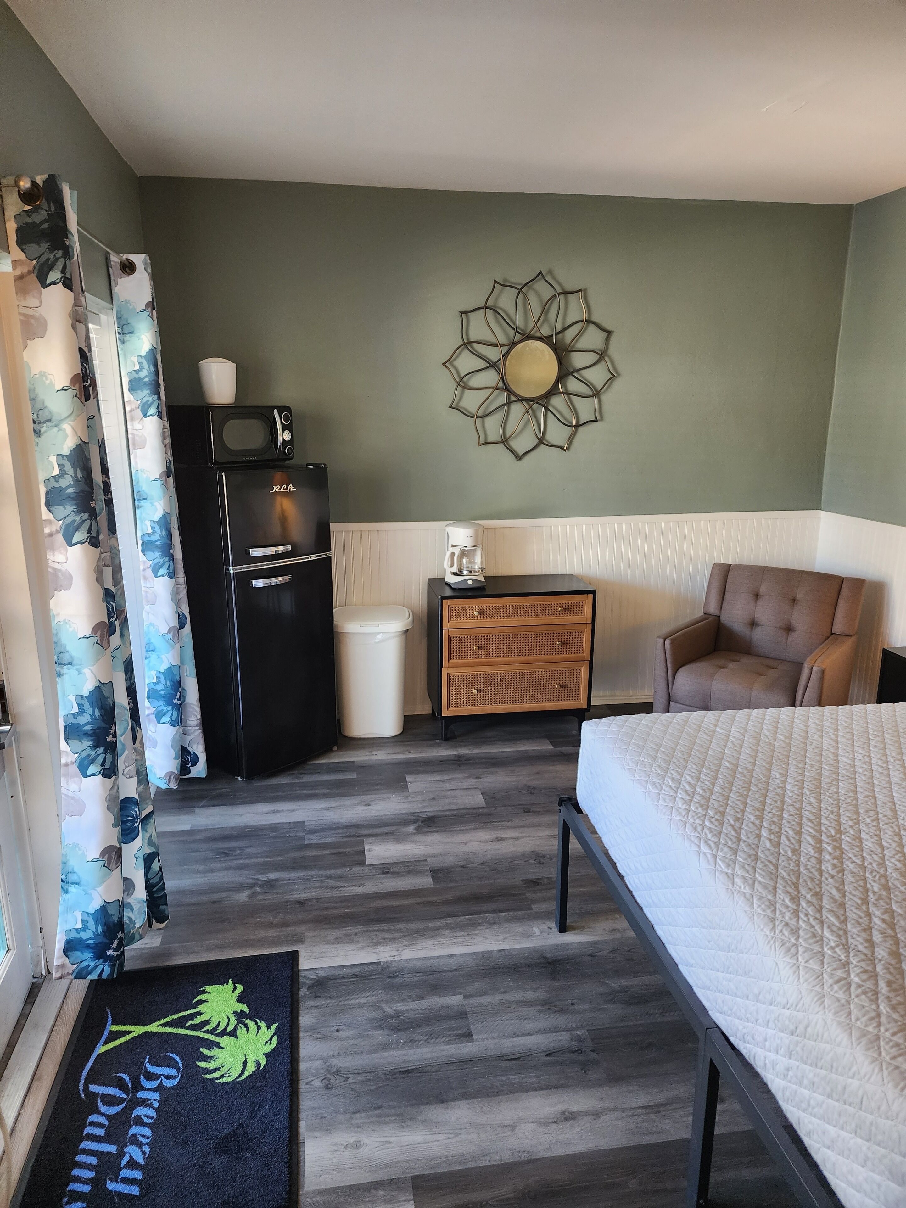 A bedroom with a bed, a dresser, a microwave, a coffee maker, and a trash can.