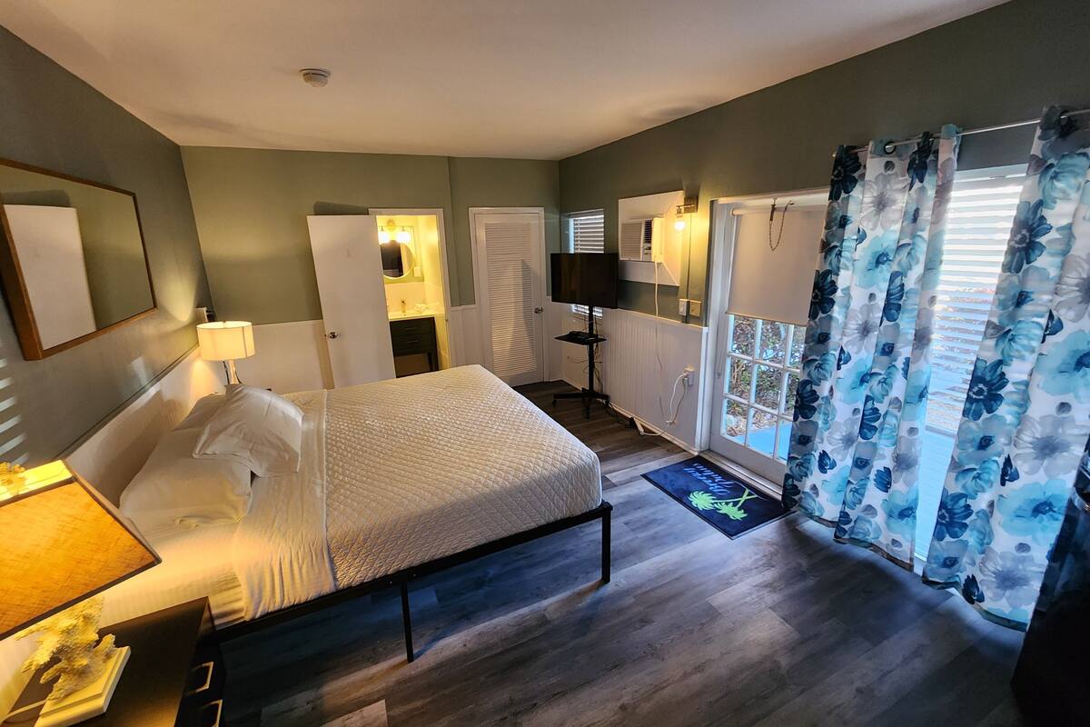 Une chambre à coucher avec un lit, une lampe de chevet, une commode et une fenêtre avec des rideaux.