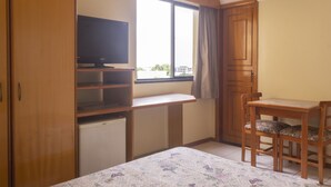 A bedroom with a bed, a desk, a chair, a television, and a window.