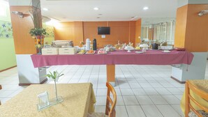 A dining area with a long table covered in a purple tablecloth, surrounded by chairs and various food items.