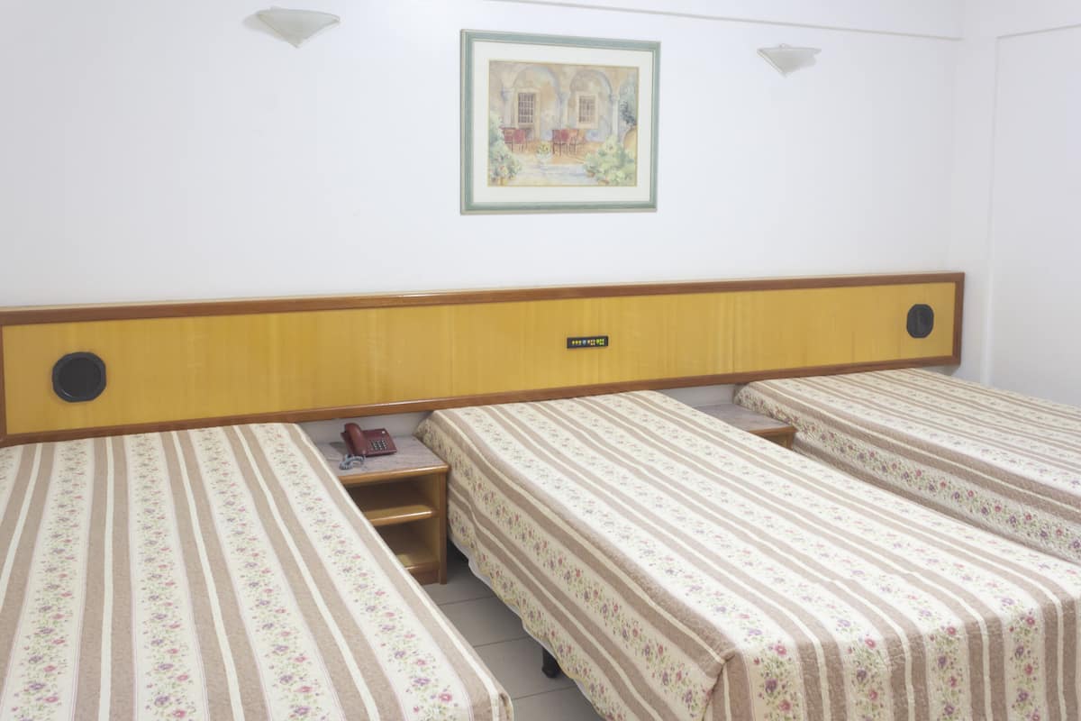 A hotel room with three single beds, a wooden headboard, a small bedside table with a telephone, and a framed picture on the wall.