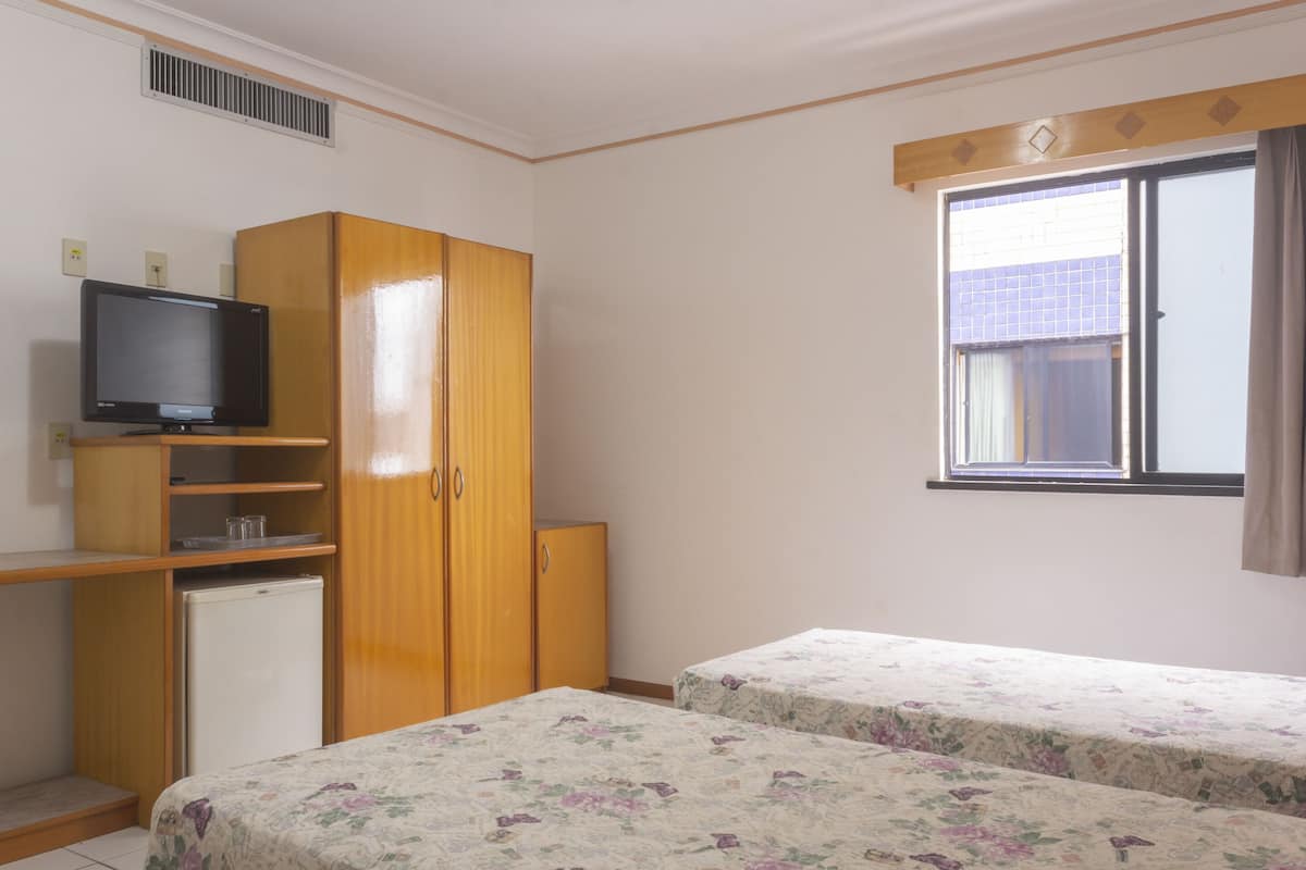 A bedroom with two beds, a TV, a wardrobe, and a window with curtains.