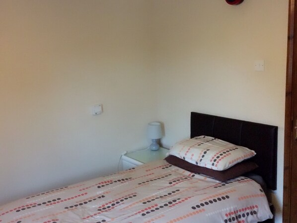 A small, simple room with a bed, a nightstand, and a lamp. - The Lodge Guesthouse (Rochester)