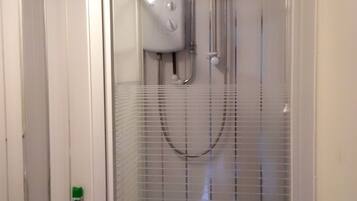 Ducha con mampara de vidrio, panel de control y cabezal de ducha manual.