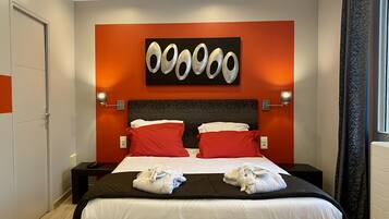 A modern hotel room with a large bed, red and white pillows, and a unique wall art piece.