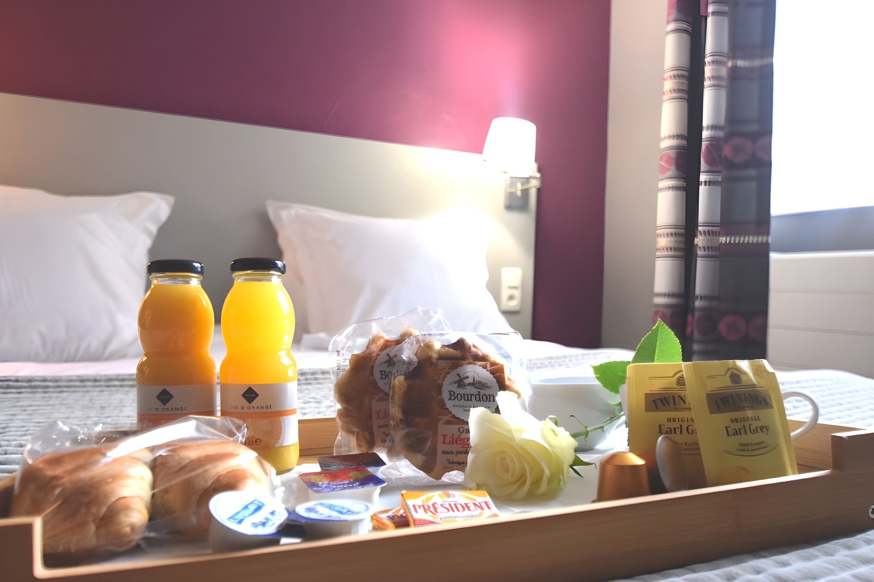 Ein Frühstücksbrett mit Croissants, Saft, Kaffee und Gebäck auf einem Hotelbett.