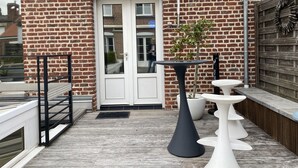 Fachada de ladrillo con una puerta blanca, una pequeña planta en maceta y muebles de exterior modernos.