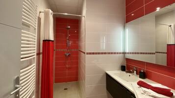A modern bathroom with a red shower, white tiles, a large mirror, and a white sink with a red towel.