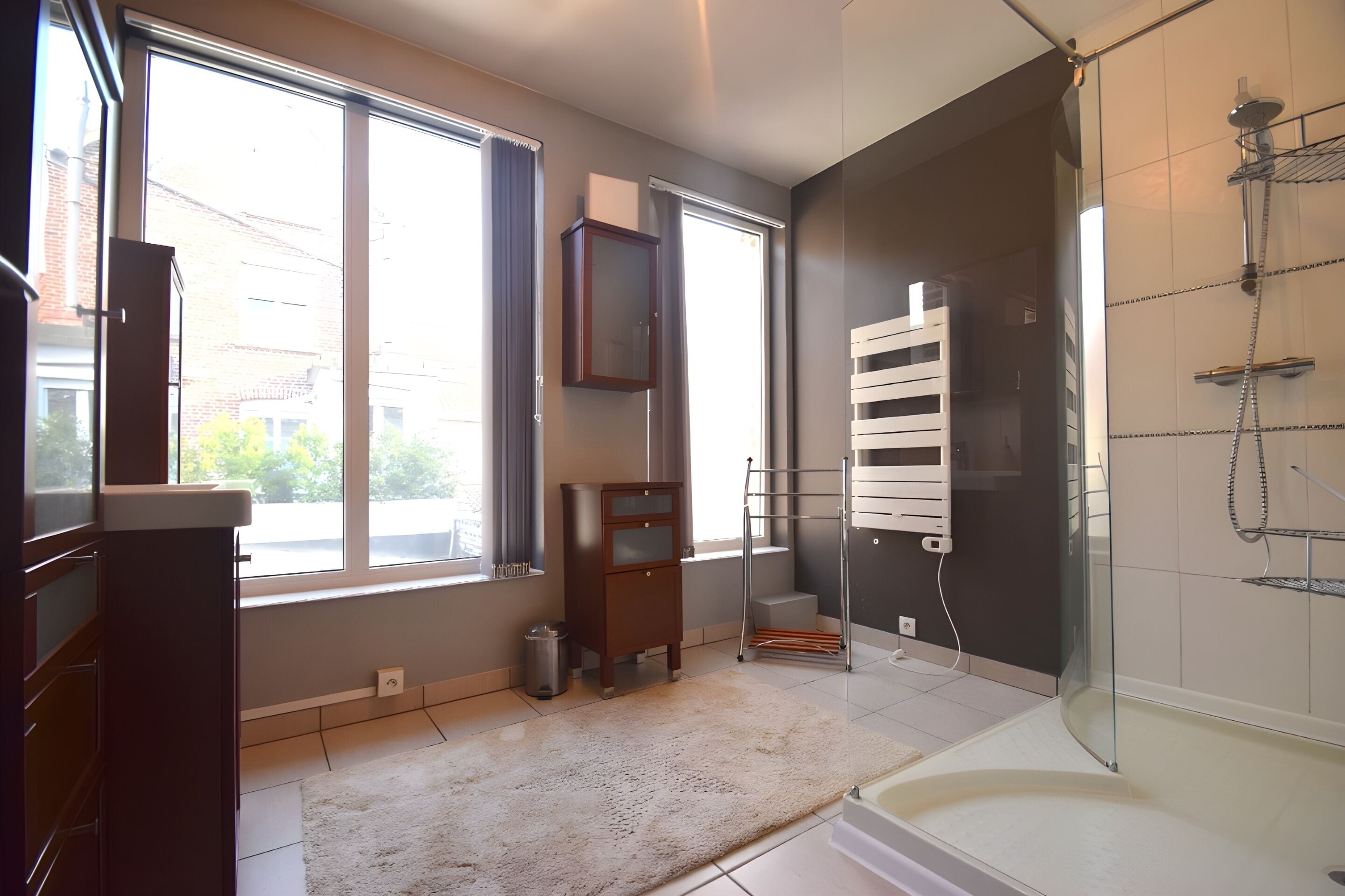 Un baño moderno con ducha envuelta en vidrio, inodoro empotrado y un amplio ventanal que proporciona luz natural.