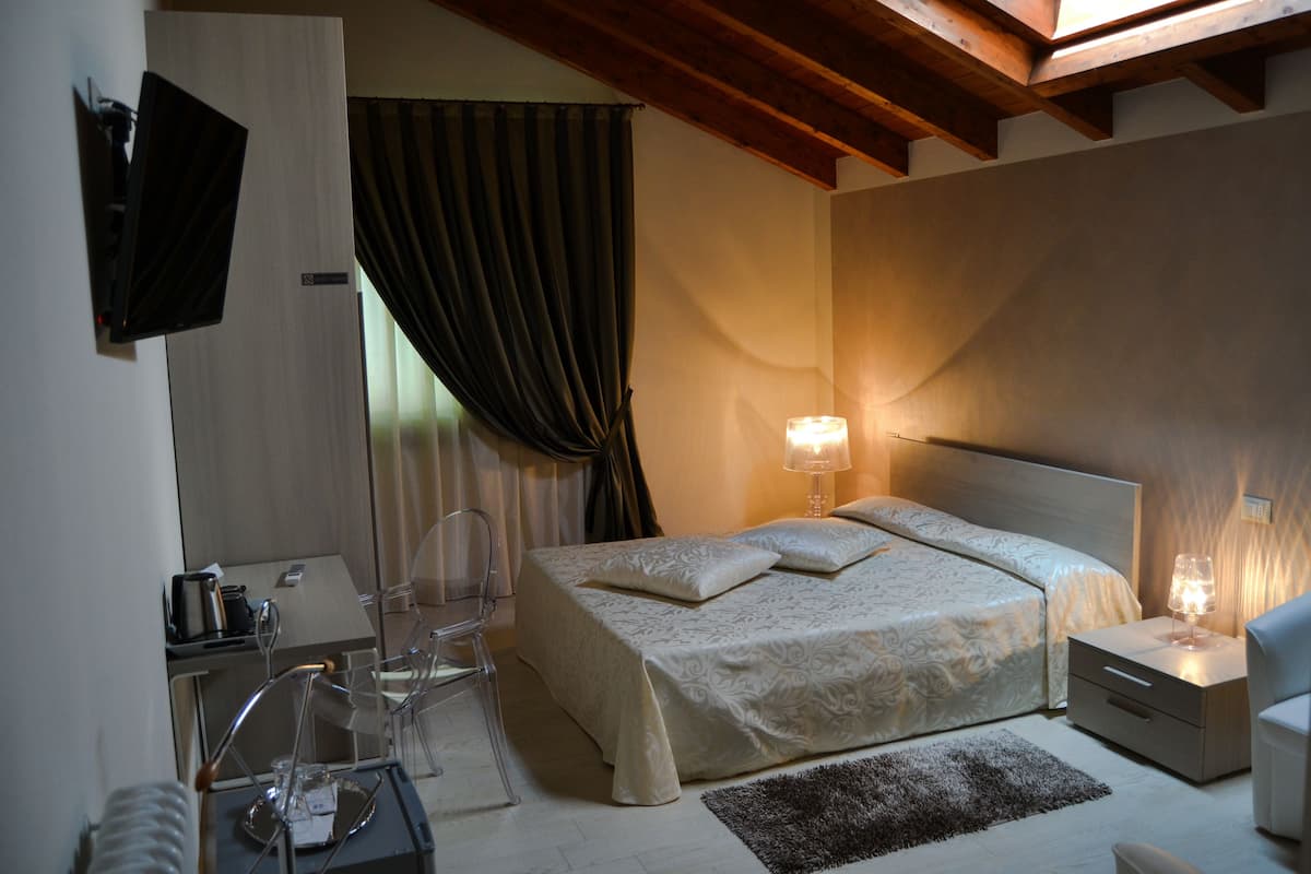 Une chambre d’hôtel moderne dotée d’un grand lit, de tables de chevet, d’un téléviseur fixé au mur et d’un bureau avec une chaise.