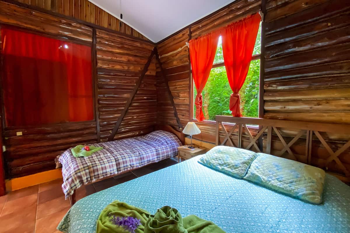 A cabin with two beds, one with a plaid bedspread and the other with a blue bedspread.