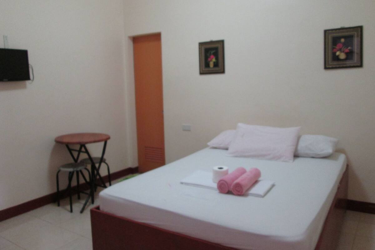 Una cama individual con colchón blanco, una mesita redonda y dos cuadros en la pared.