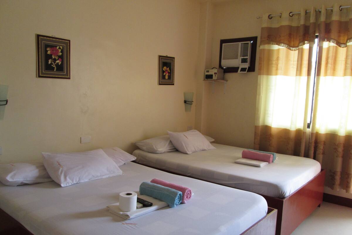 Habitación de hotel con dos camas individuales, aire acondicionado de pared y ventana con cortinas.