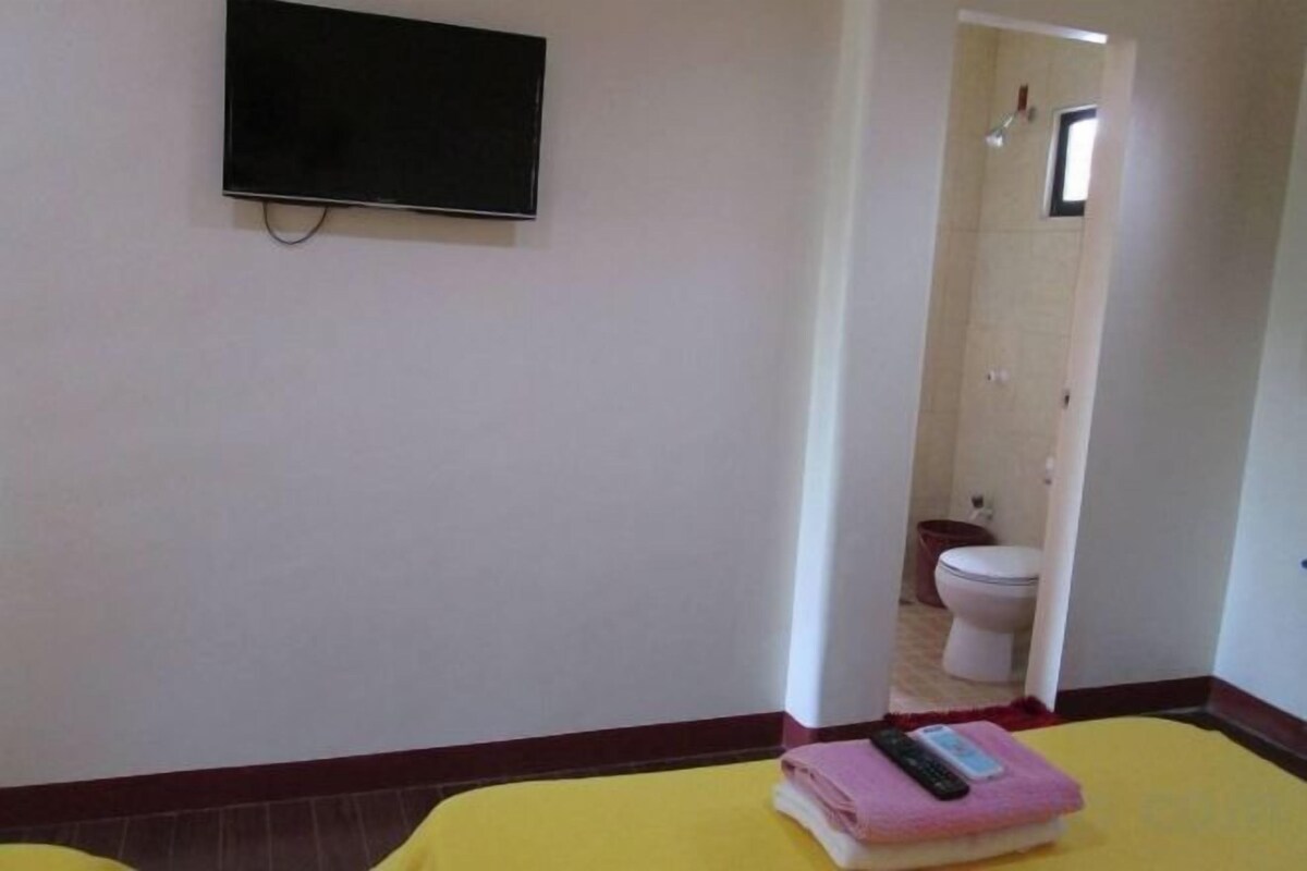 A hotel room with a bed, a television on the wall, and a bathroom visible through an open door.