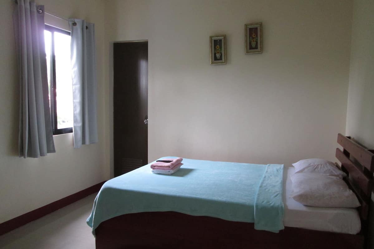 A bedroom with a bed, a window with curtains, a door, and two framed pictures on the wall.