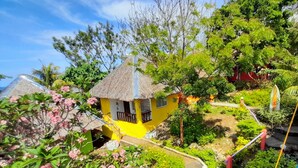 A yellow house with a thatched roof, surrounded by lush greenery and flowering plants. - Boracay Water World Resort (Boracay Island)