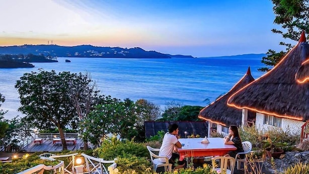 A dining area with a table and chairs overlooking a body of water, with a thatched-roof structure nearby. - Boracay Water World Resort (Boracay Island)