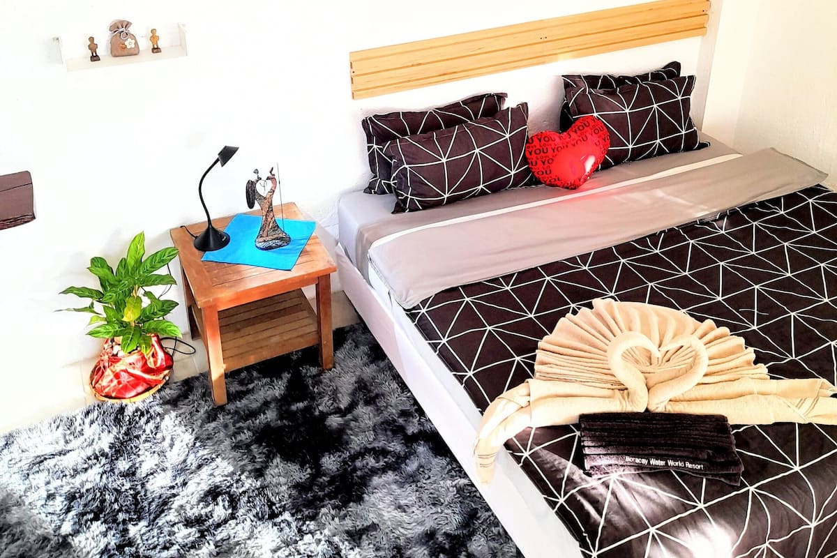Une chambre à coucher avec un lit, une table de chevet, une lampe, une plante et un mur décoré de tableaux encadrés.
