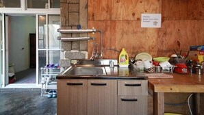 Una cocina con un lavamanos de acero inoxidable, armarios de madera y protector contra salpicaduras de piedra. Hay un cartel solicitando a los huéspedes que laven sus platos.