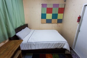 A small, neatly made bed with a white sheet and a colorful quilt hanging on the wall above it. - Urban Art Guesthouse (Seoul)