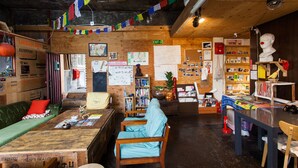 Un interior acogedor y rústico con paredes y muebles de madera, que incluye una zona de recepción, un mostrador, una estantería y un área de estar con un sofá verde y sillas de madera.