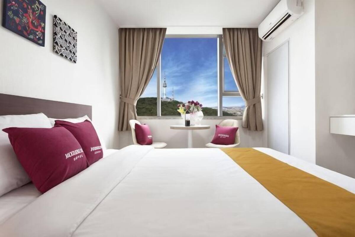 A hotel room with a bed, two chairs, a small table, and a window with curtains.