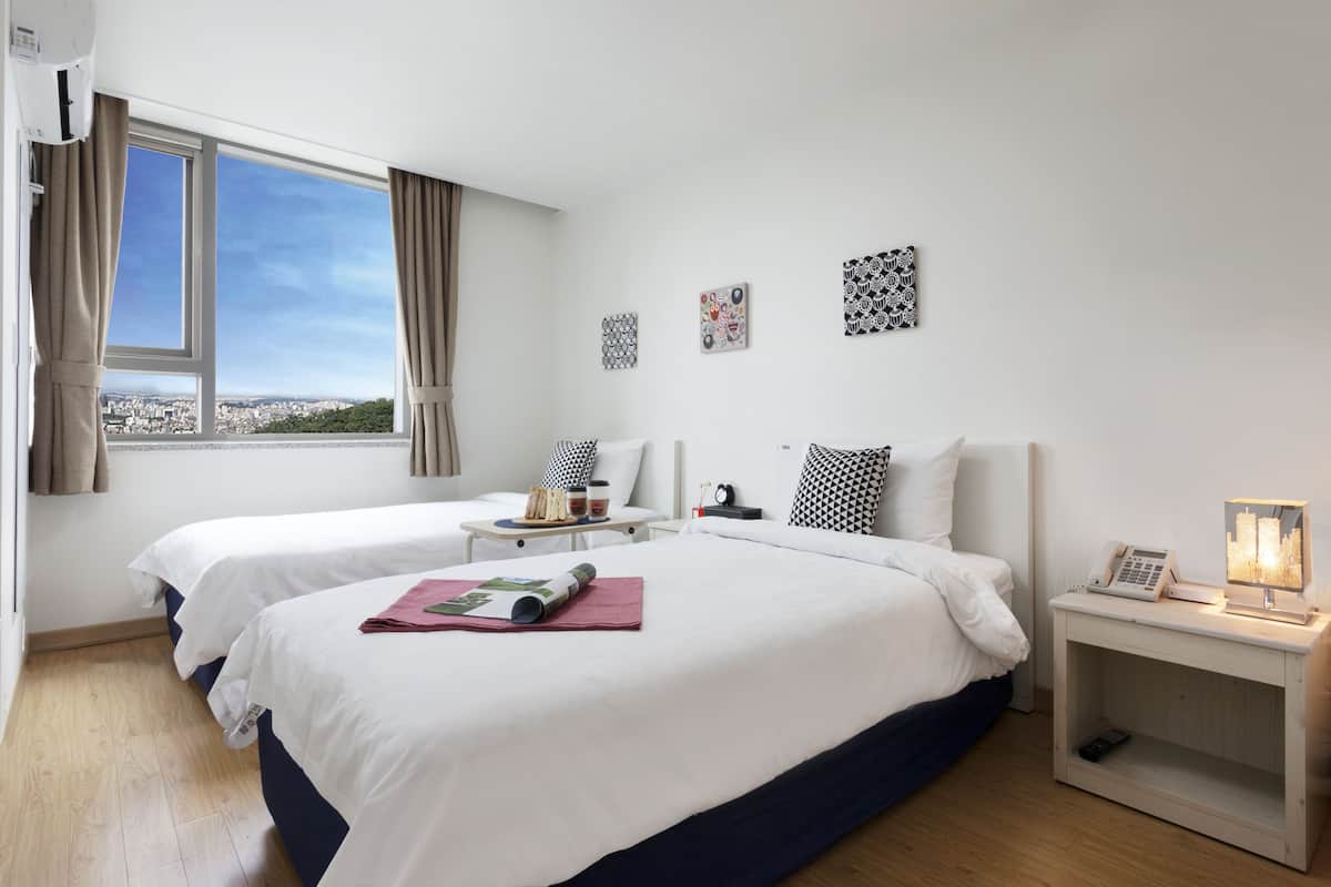 A hotel room with two beds, a bedside table with a lamp, a phone, and a nightstand with a picture frame.