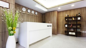 A reception desk with clocks, a vase of flowers, and a bookshelf with various items. - Hotel Morning Sky (Seoul)