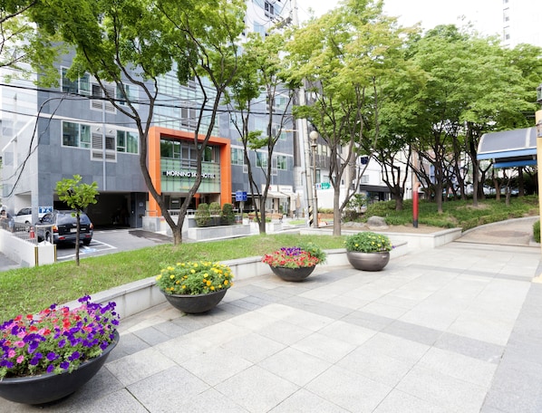 Un hotel moderno con una llamativa fachada naranja, grandes macetas de flores y un camino pavimentado.