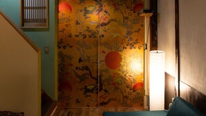 Ein Zimmer mit einer traditionellen, gleitenden Tür, die ein Naturmotiv zeigt, einer Stehlampe und einer Holztreppe.