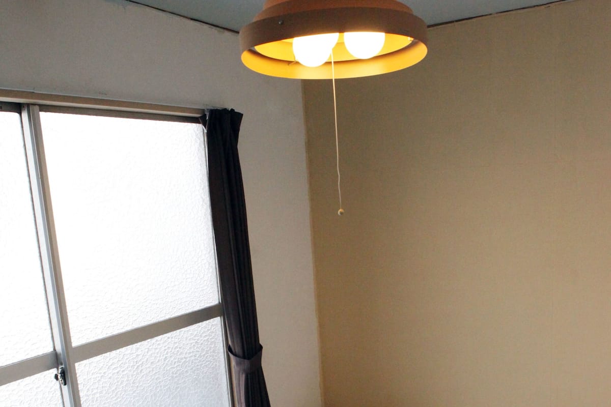 Een kamer met tatami matten, een futon bed, een verschuifbare shoji schermen en een hanglamp.