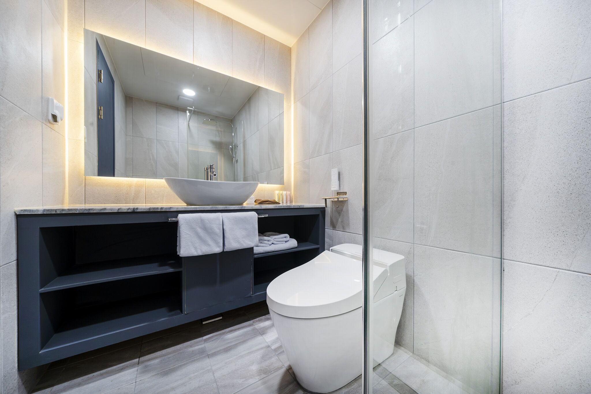 Et moderne badeværelse med et stort spejl, en skål-vask, toilet og et mørkt skab.