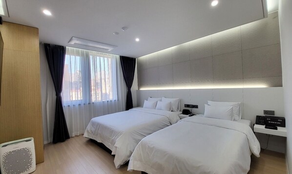 A hotel room with two beds, a bedside table with a phone, and a wall-mounted air conditioner.