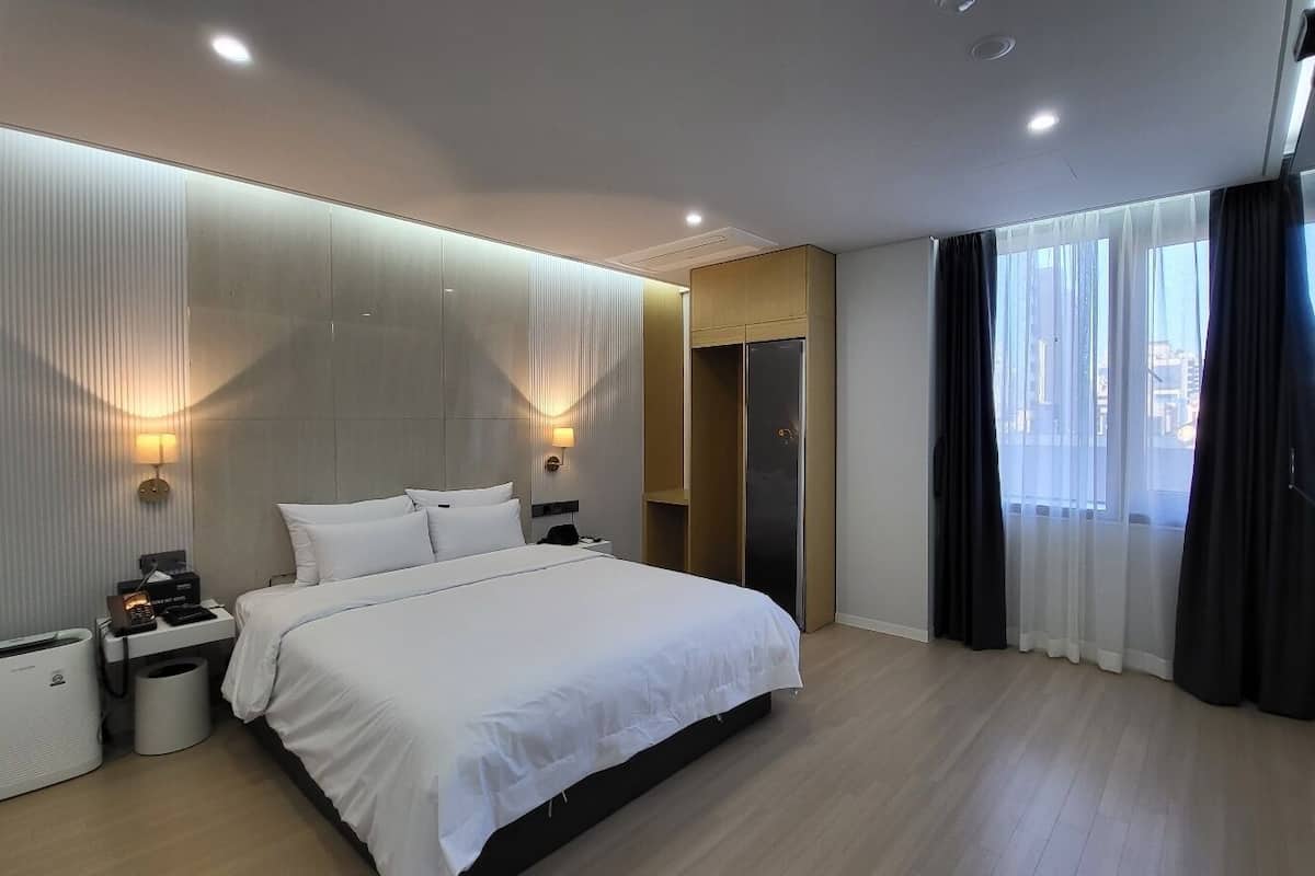 Quarto de hotel moderno com uma cama grande, luminárias de cabeceira, um guarda-roupa e uma janela ampla com cortinas.