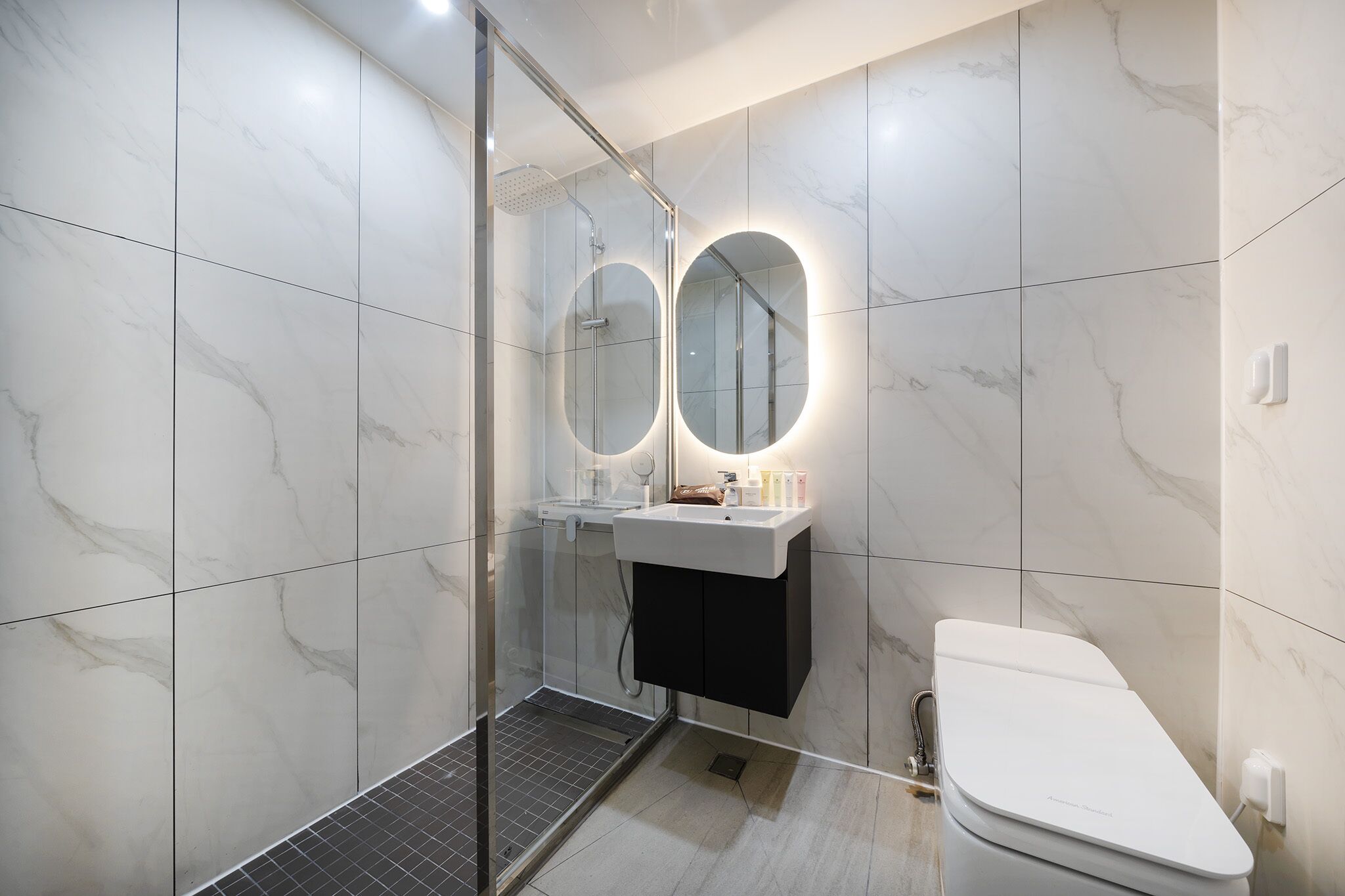 Un baño moderno con ducha envuelta en vidrio, un lavamanos blanco con espejo y un inodoro blanco.