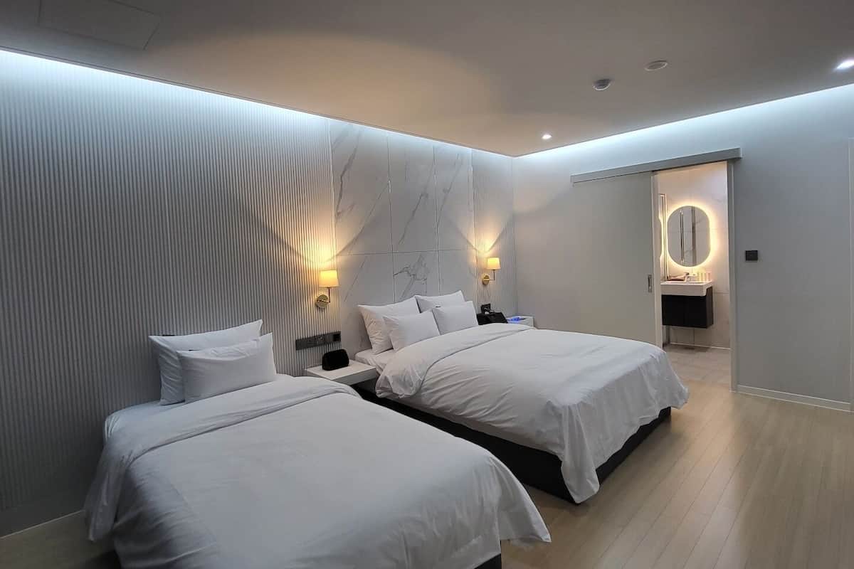 Quarto de hotel moderno com duas camas, um espelho grande e um banheiro com toucador.