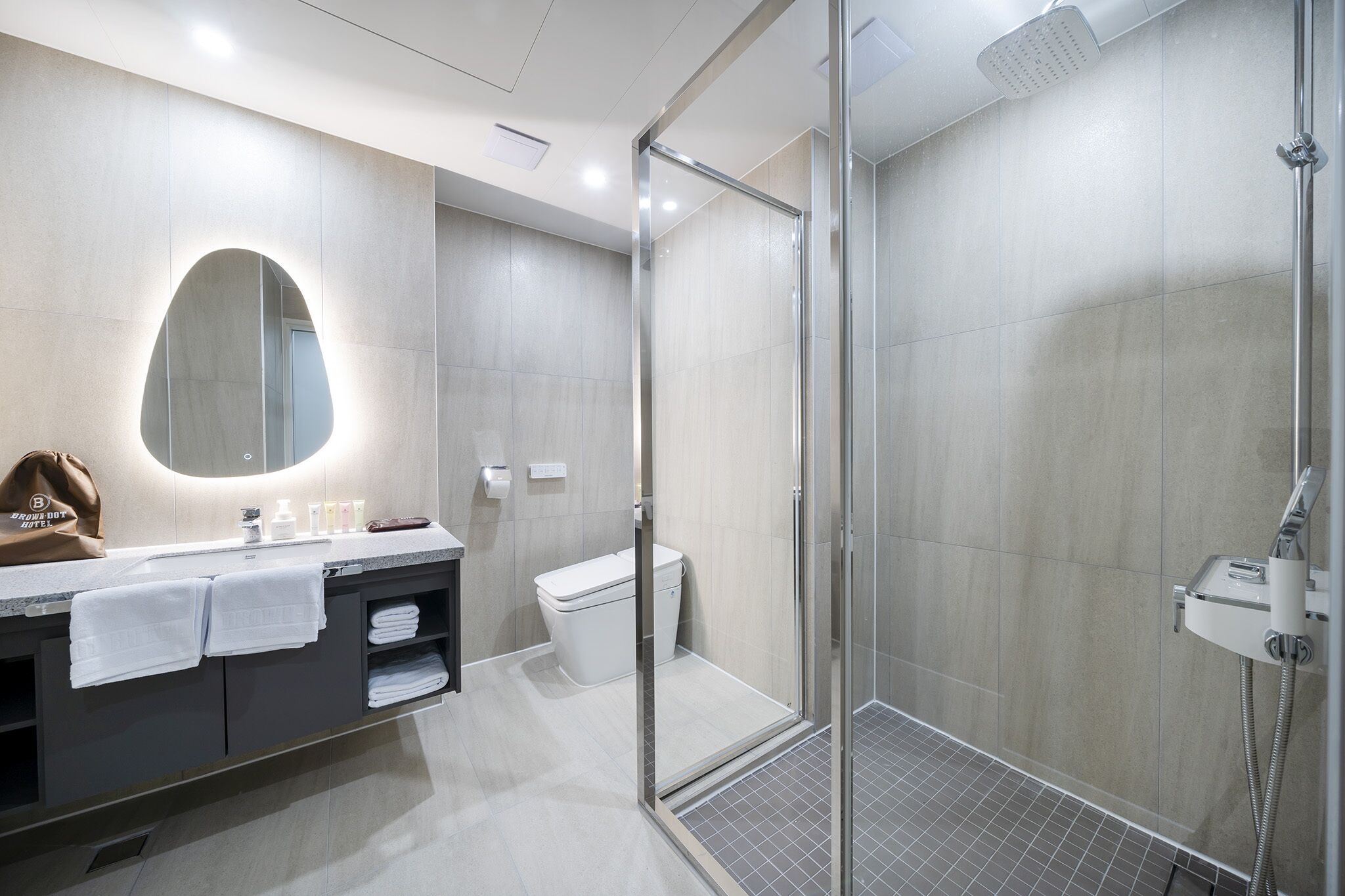 Un baño moderno con ducha envuelta en vidrio, un espejo grande y un tocador con toallas.