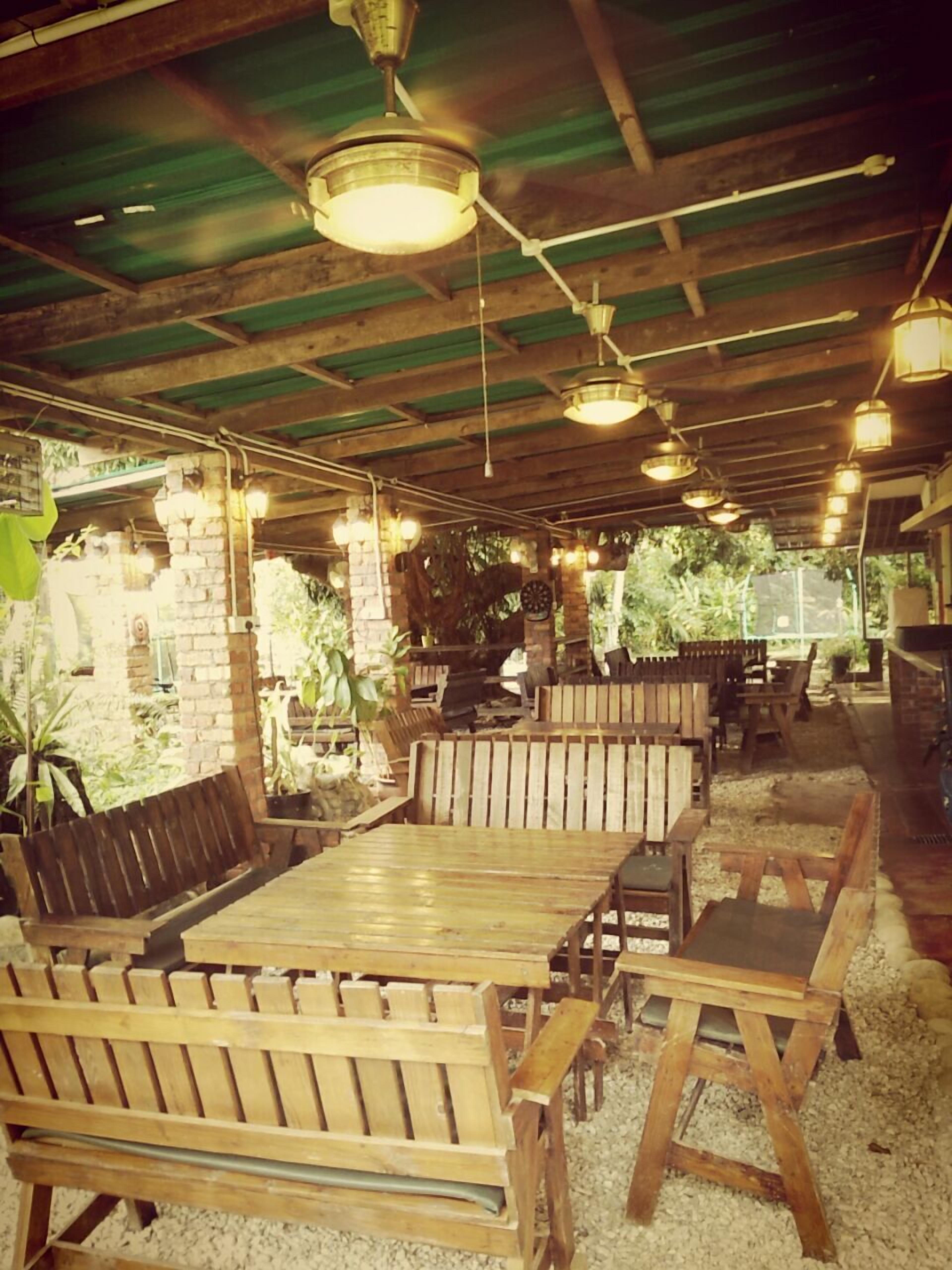 An outdoor dining area with wooden benches and tables, surrounded by greenery.