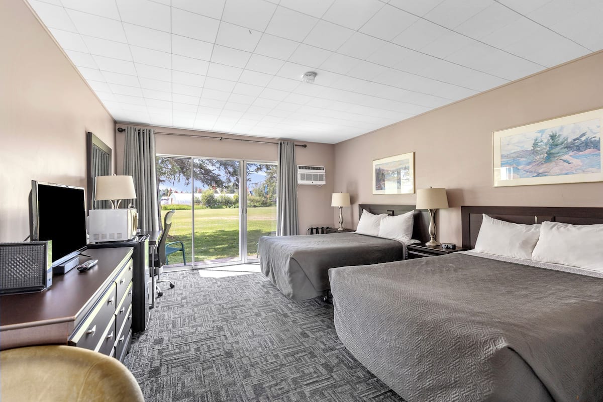A hotel room with two beds, a desk with a computer, a TV, and a large window with a view of the outdoors.