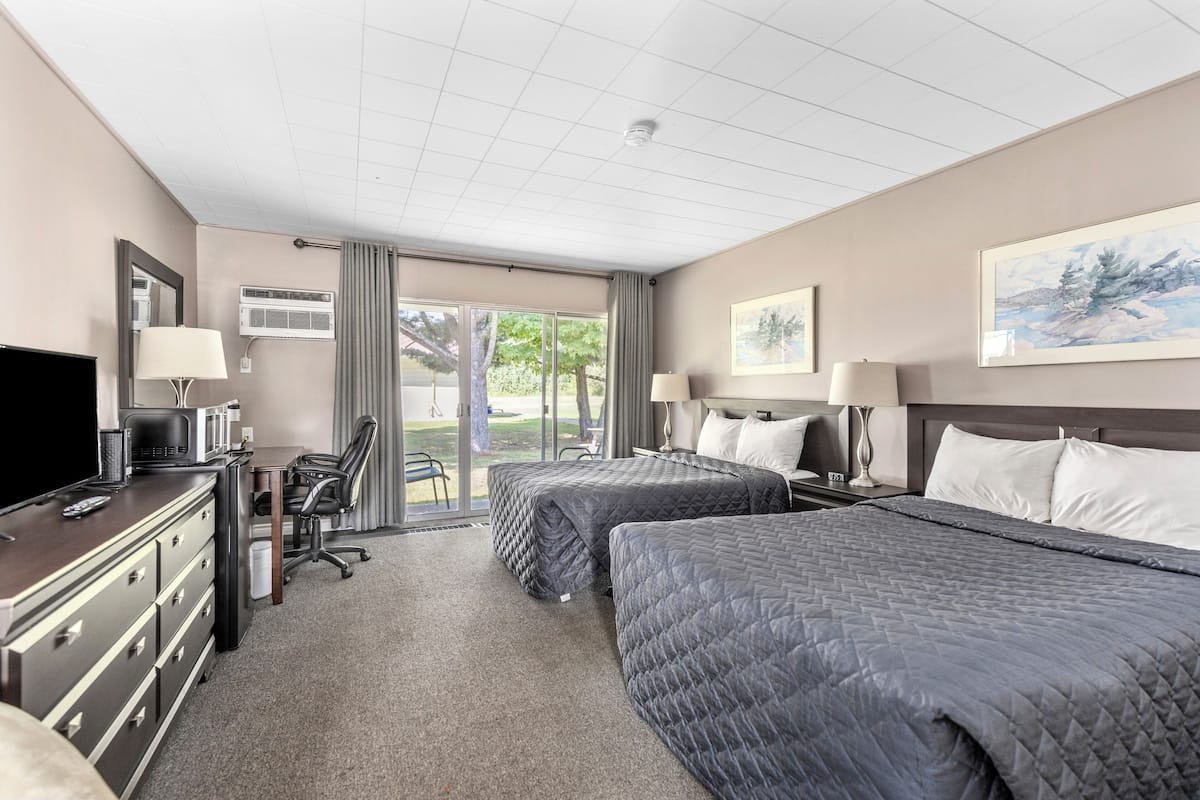 A hotel room with two beds, a desk with a computer, a TV, and a large window with a view of greenery.