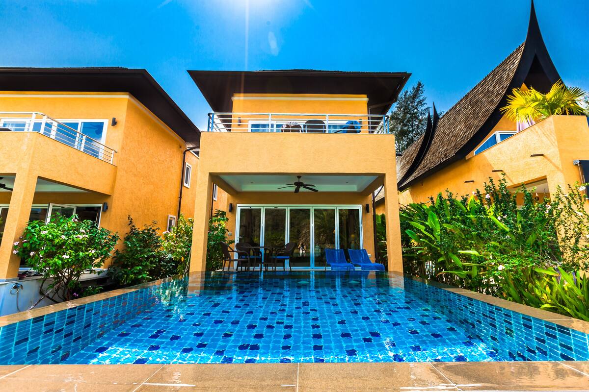 A hotel with a swimming pool, outdoor seating, and a covered area with a ceiling fan.