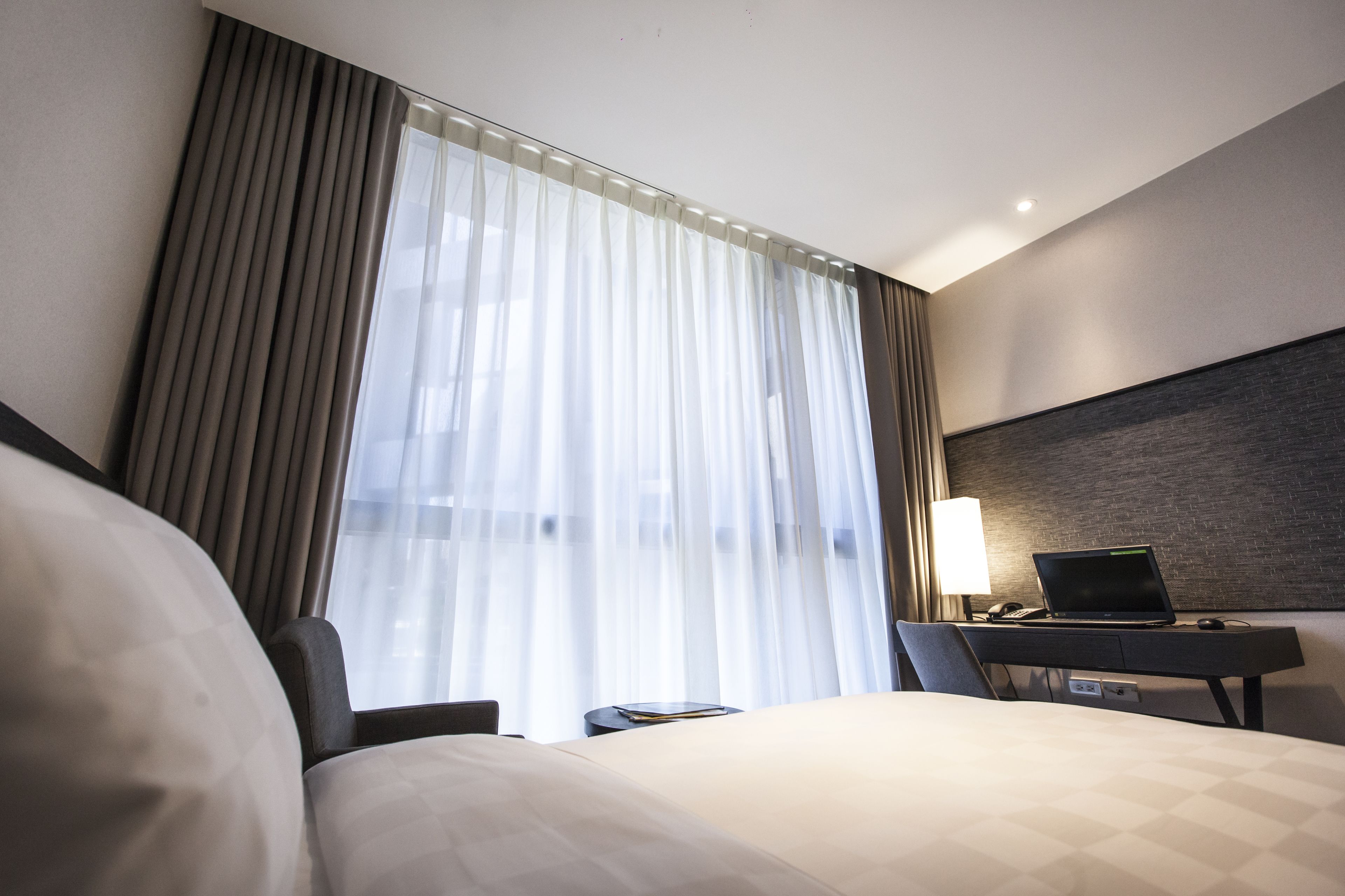 Una habitación de hotel con cama, escritorio y laptop, además de una lámpara.