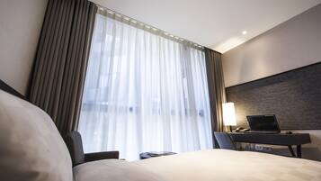 Una habitación de hotel con cama, escritorio y laptop, además de una lámpara.
