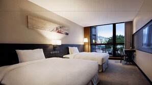 Une chambre d’hôtel avec deux lits, une grande fenêtre, un bureau et un tableau au mur.
