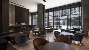 Un espace de détente intérieur moderne, doté de tables et de chaises, de grandes fenêtres et d’un comptoir de bar.
