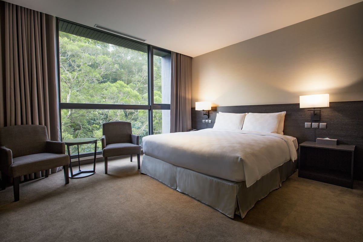 Een hotelkamer met een groot bed, twee fauteuils, een tafeltje en een nachtkastje met een lamp.