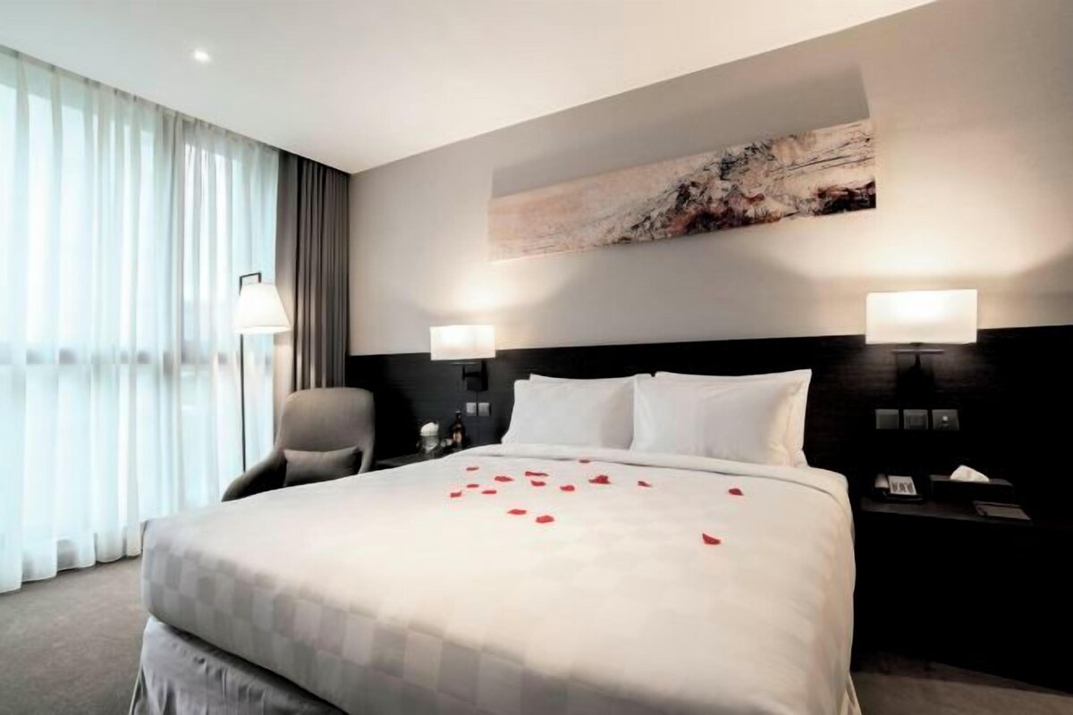Ein Hotelzimmer mit einem großen Bett, zwei Nachttischlampen, einem Sessel, einem Schreibtisch mit Lampe und einem Bild an der Wand.