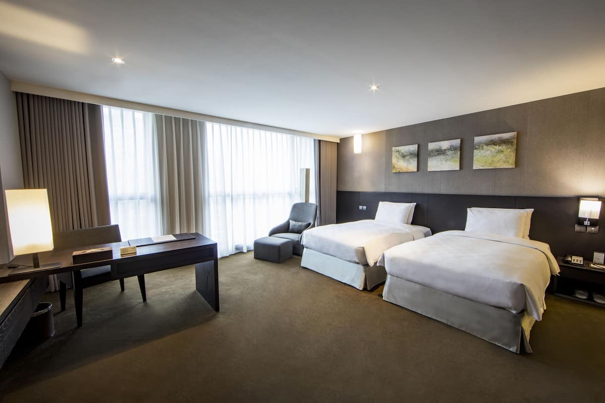 Een hotelkamer met twee bedden, een bureau, een stoel en een groot raam met gordijnen.