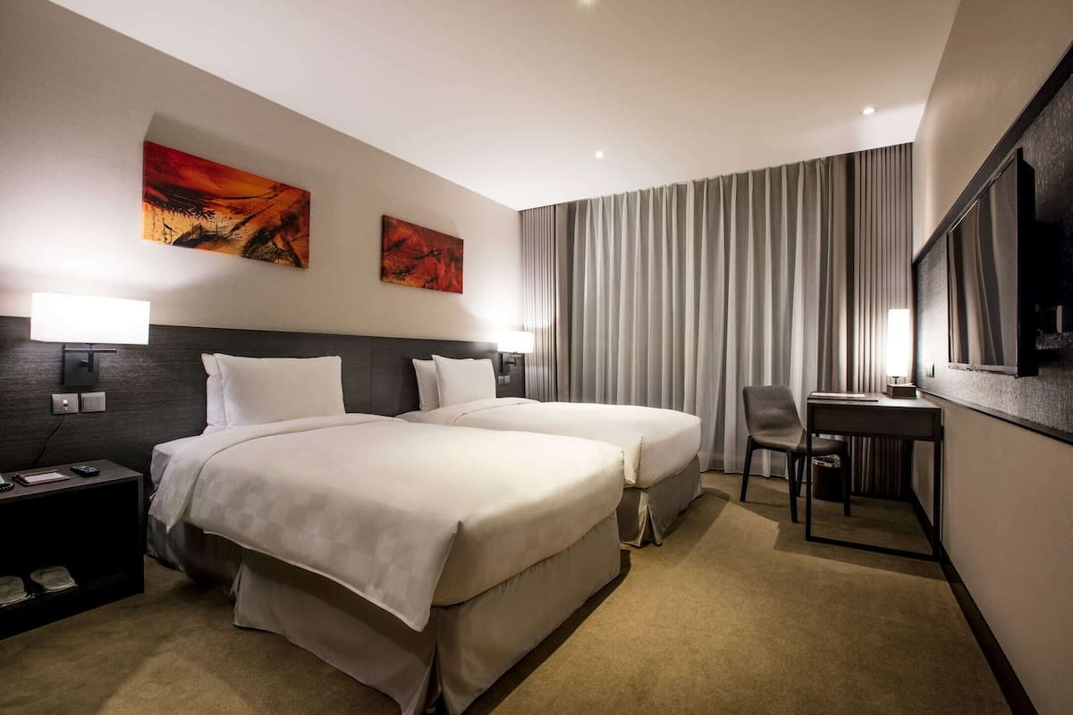 Een hotelkamer met twee bedden, een bureau, een stoel, een televisie en kunst aan de muur.